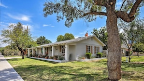 A single-story house with a porch, surrounded by a well-maintained lawn and trees. - Central Phoenix Home < 3 Mi to Downtown! (Phoenix)