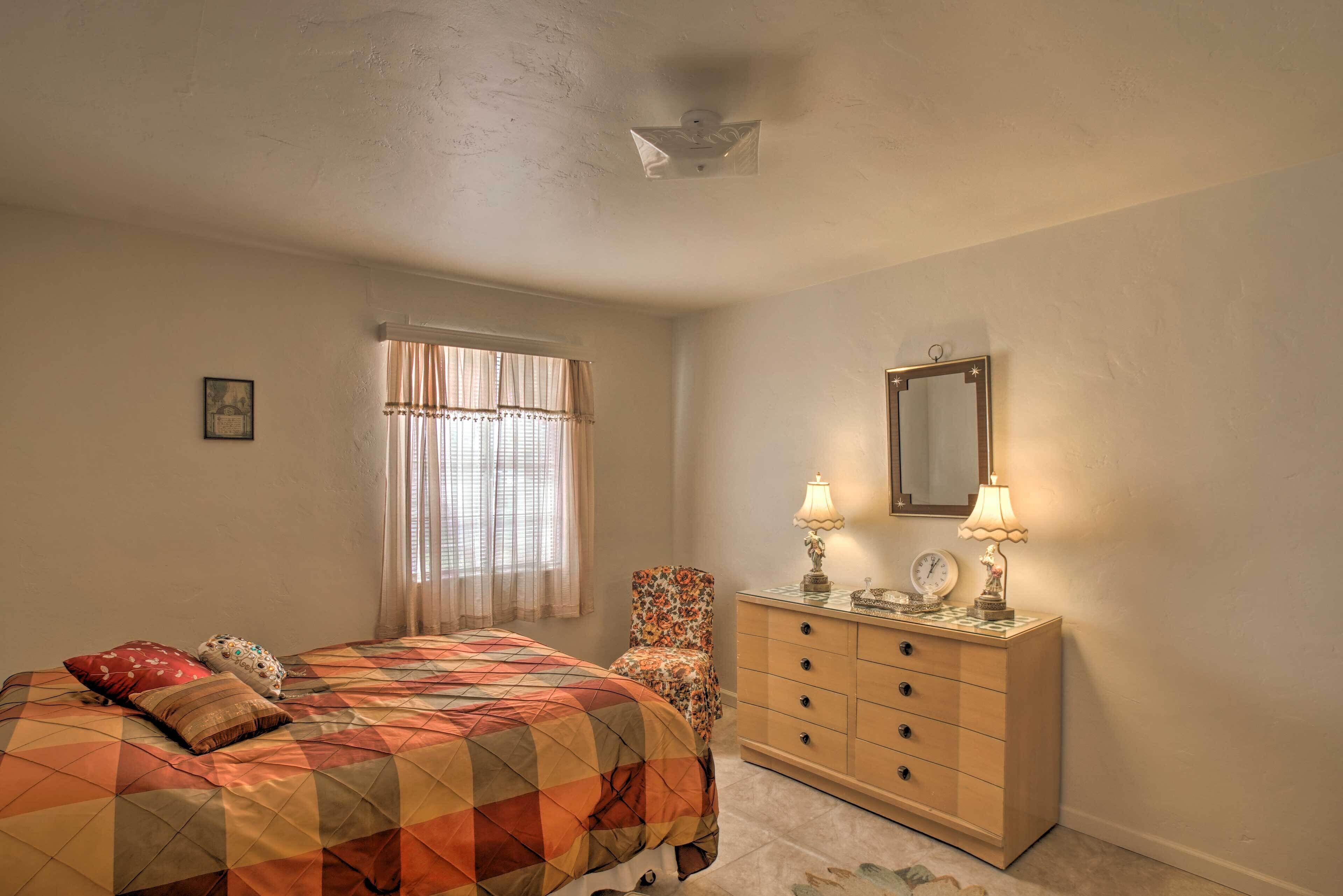 A bedroom with a bed, a dresser, a chair, a mirror, and a window with curtains.