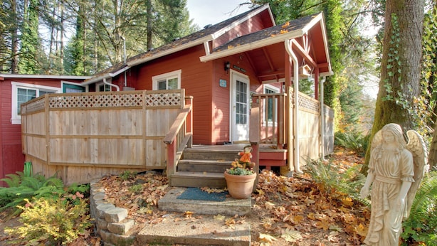 Une cabane rouge avec une terrasse en bois, un porche et une statue d’un ange.