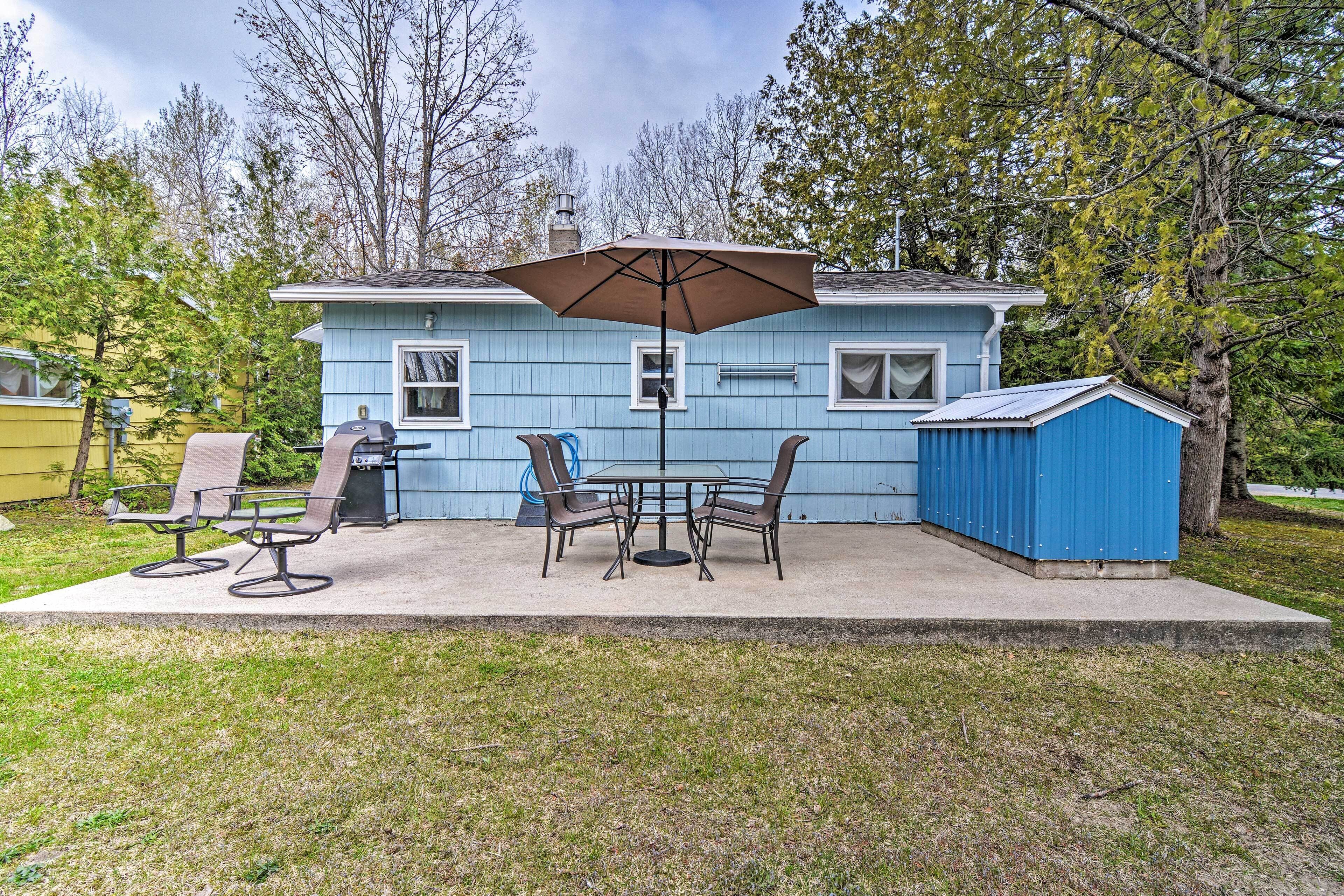 A blue house with a patio, a table and chairs, an umbrella, and a shed.