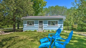 Une petite cabane bleu clair, dotée d’une porte et de fenêtres, entourée d’une cour verdoyante et d’arbres.