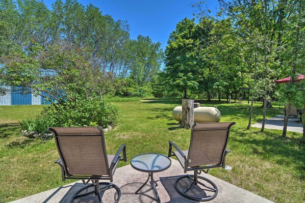 An outdoor seating area with two chairs and a table, surrounded by a grassy lawn and trees.