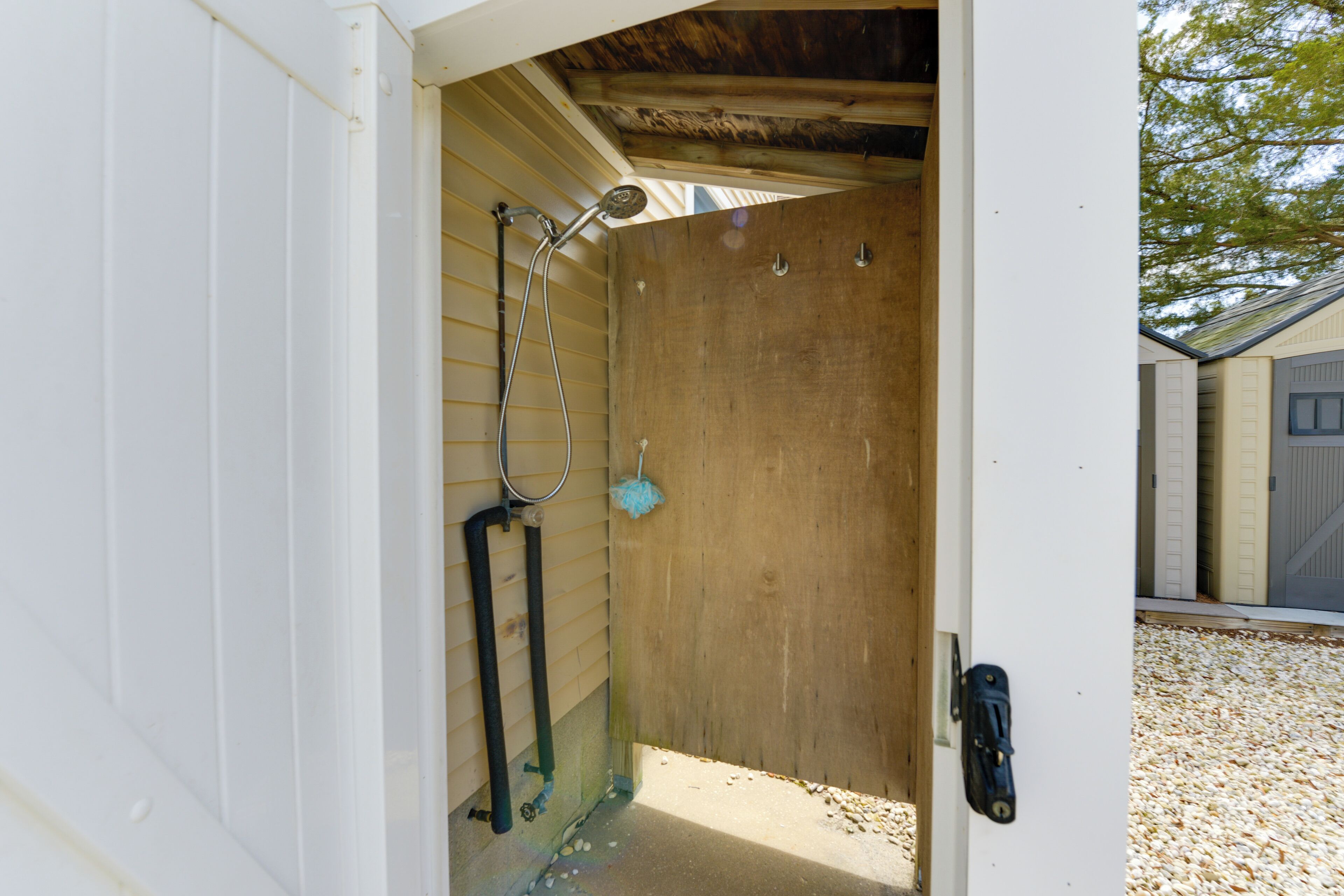 A wooden shed with a metal door, a showerhead, and a mop.