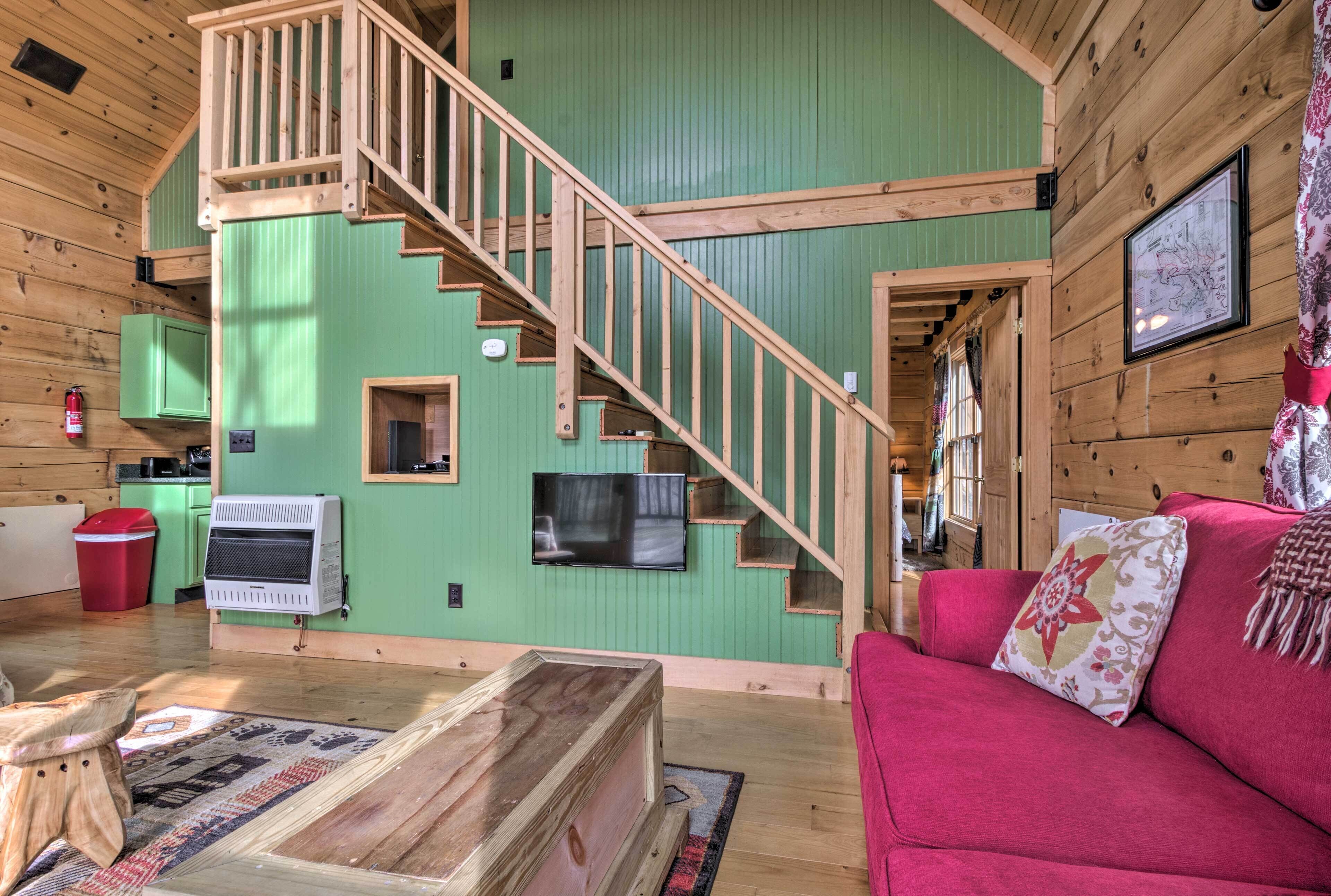 A cabin interior with a wooden staircase, a red couch, a television, and a fireplace.