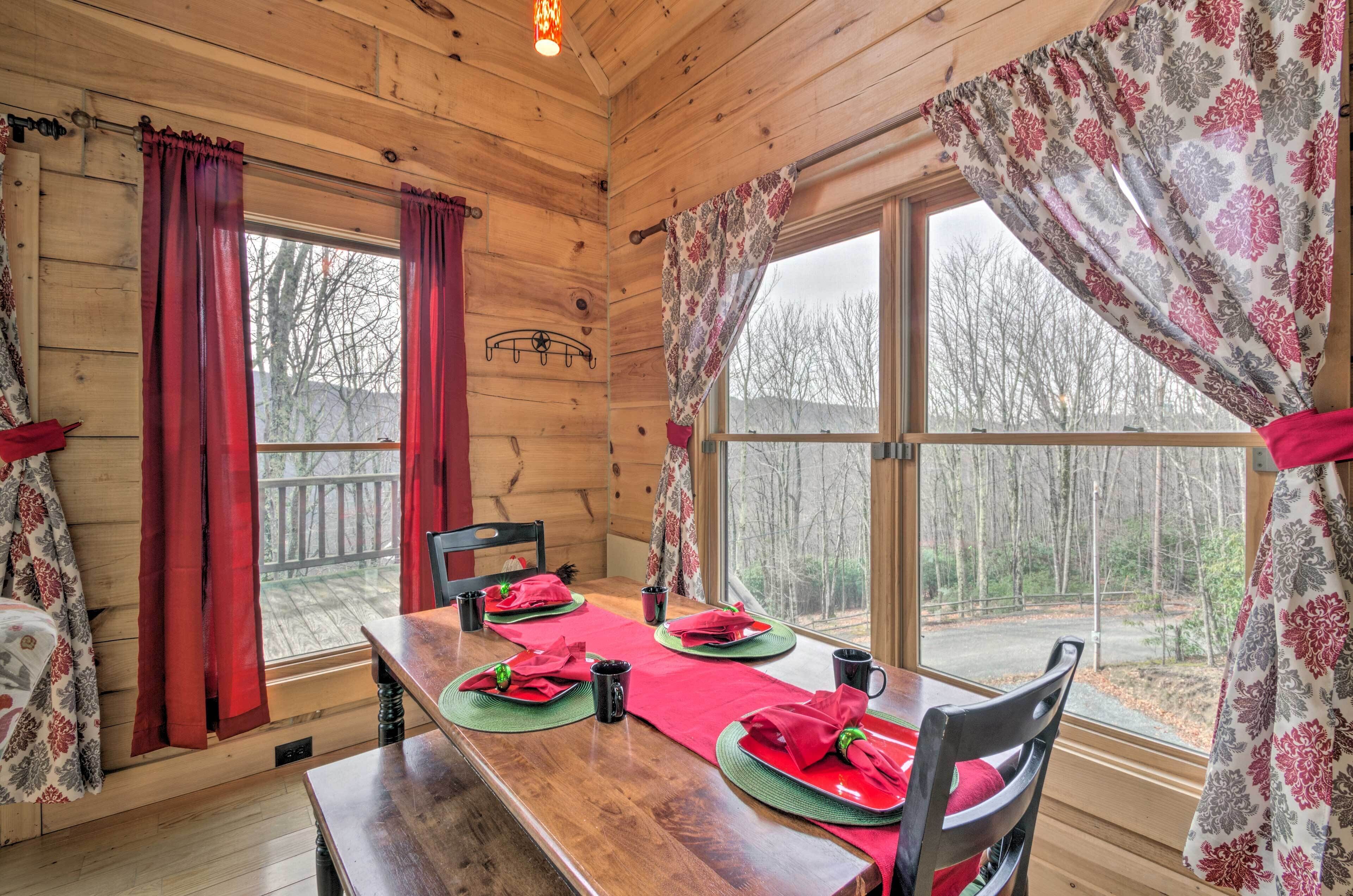Une salle à manger aménagée dans une cabane en bois, avec une table dressée pour quatre personnes, des rideaux rouges et une vue sur les arbres à l’extérieur.