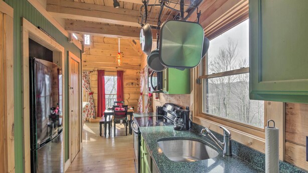 Interior de una cabaña de madera con cocina que incluye encimera de granito, pileta de acero inoxidable y ollas colgantes.