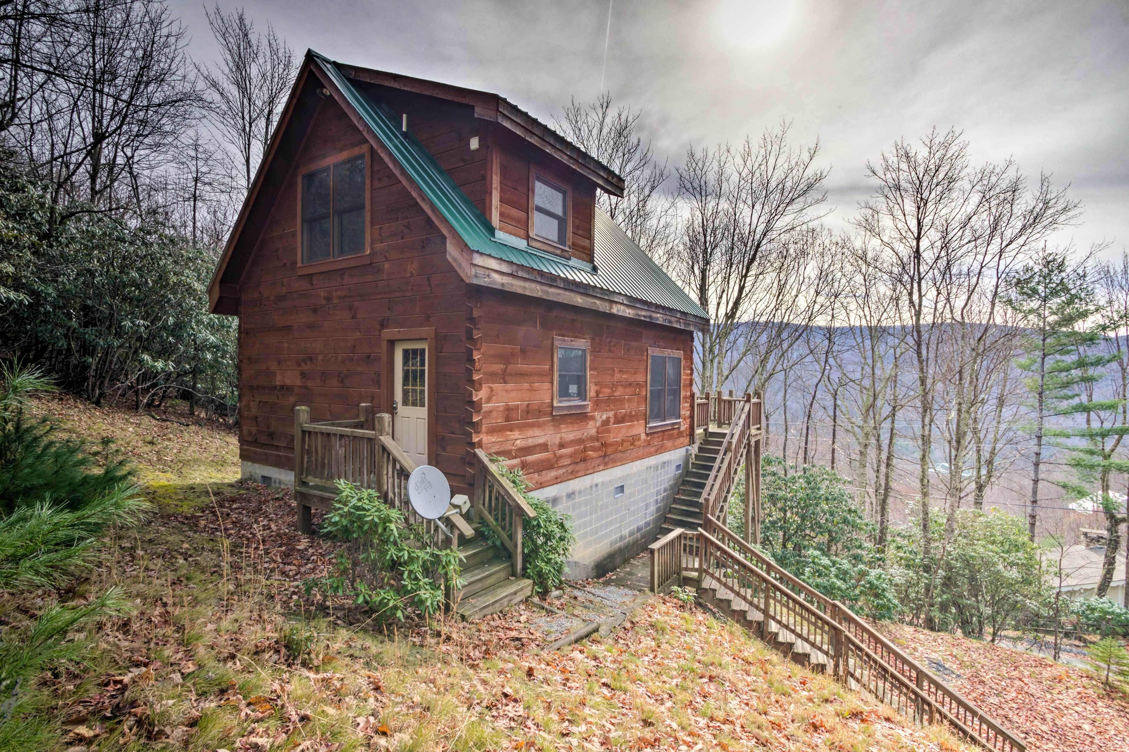 A wooden cabin with a steep staircase, a satellite dish, and a view of trees and mountains.