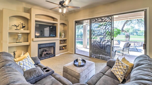 A living room with a fireplace, a ceiling fan, and a sliding glass door leading to an outdoor patio. - Pool & Putting Green: Goodyear Home on Golf Course (Goodyear)