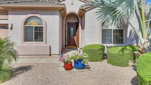 A house with a symmetrical facade, a central entrance, and a well-maintained front yard with a palm tree and neatly trimmed hedges. - Pool & Putting Green: Goodyear Home on Golf Course (Goodyear)