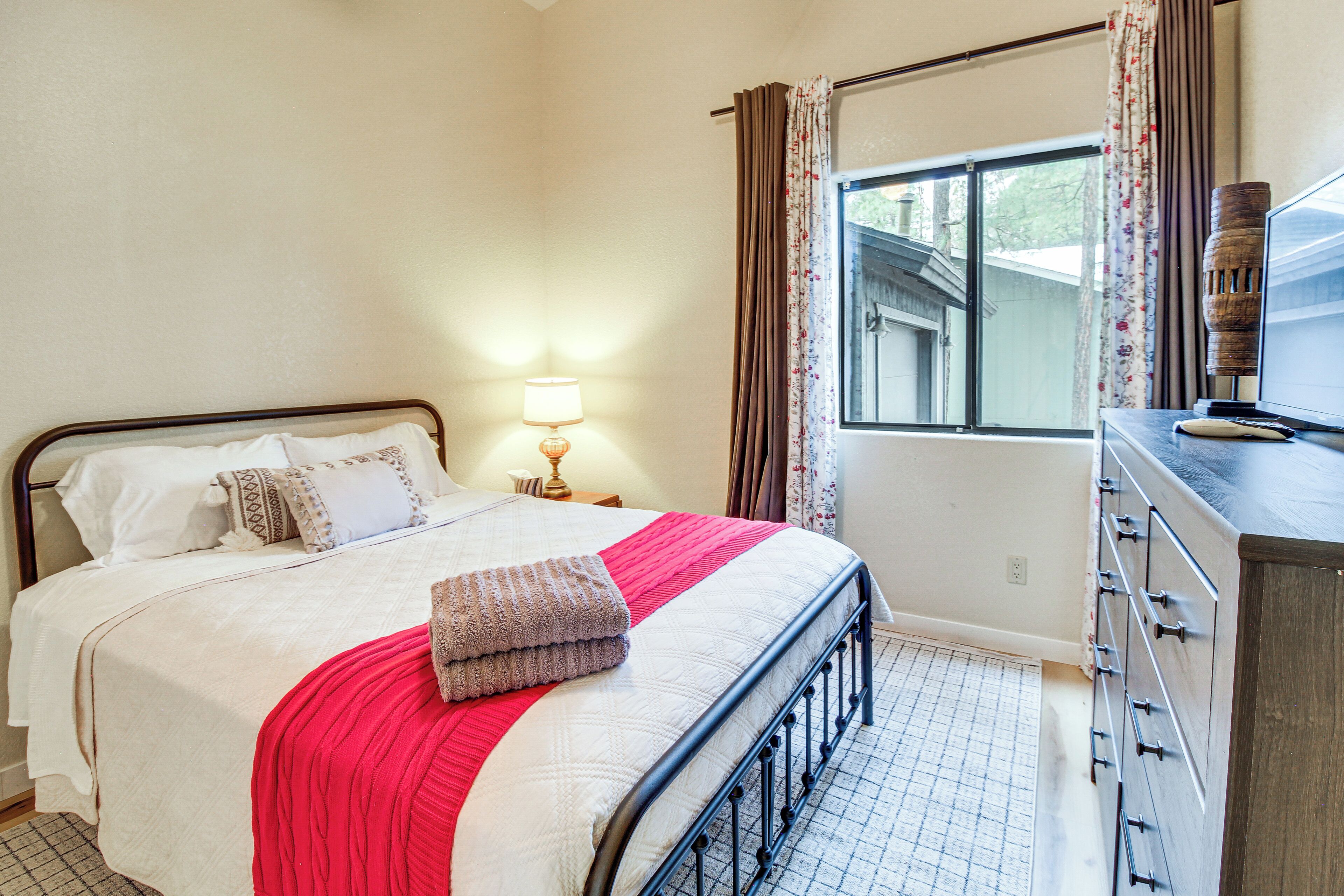 A bedroom with a bed, a nightstand, a lamp, a dresser, and a window with curtains.