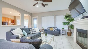 Ein geräumiges Wohnzimmer mit Kamin, Deckenventilator und einem durch einen Bogen sichtbaren Küchenbereich.