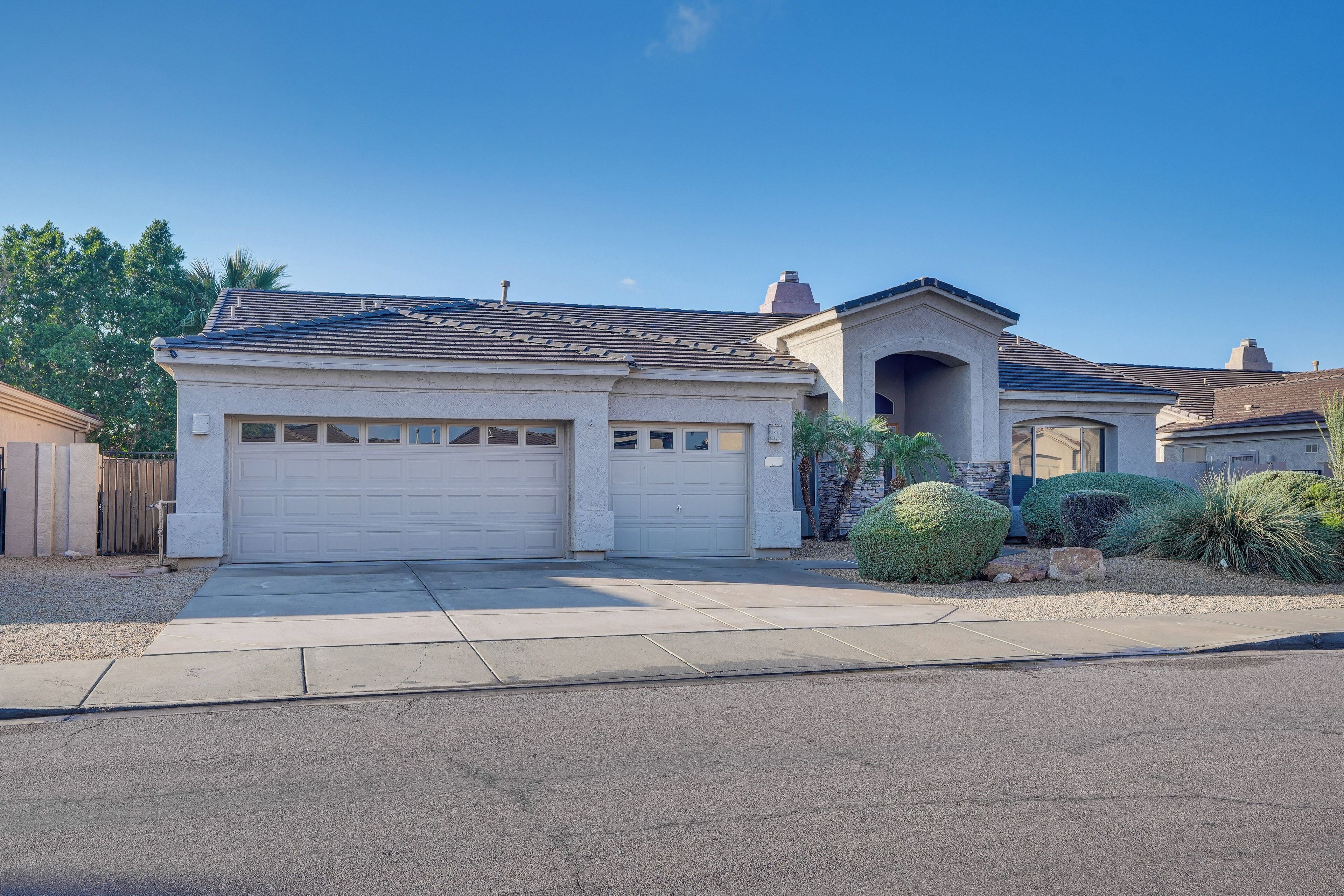 A residential house with a garage, a driveway, and landscaped garden with shrubs and a palm tree.