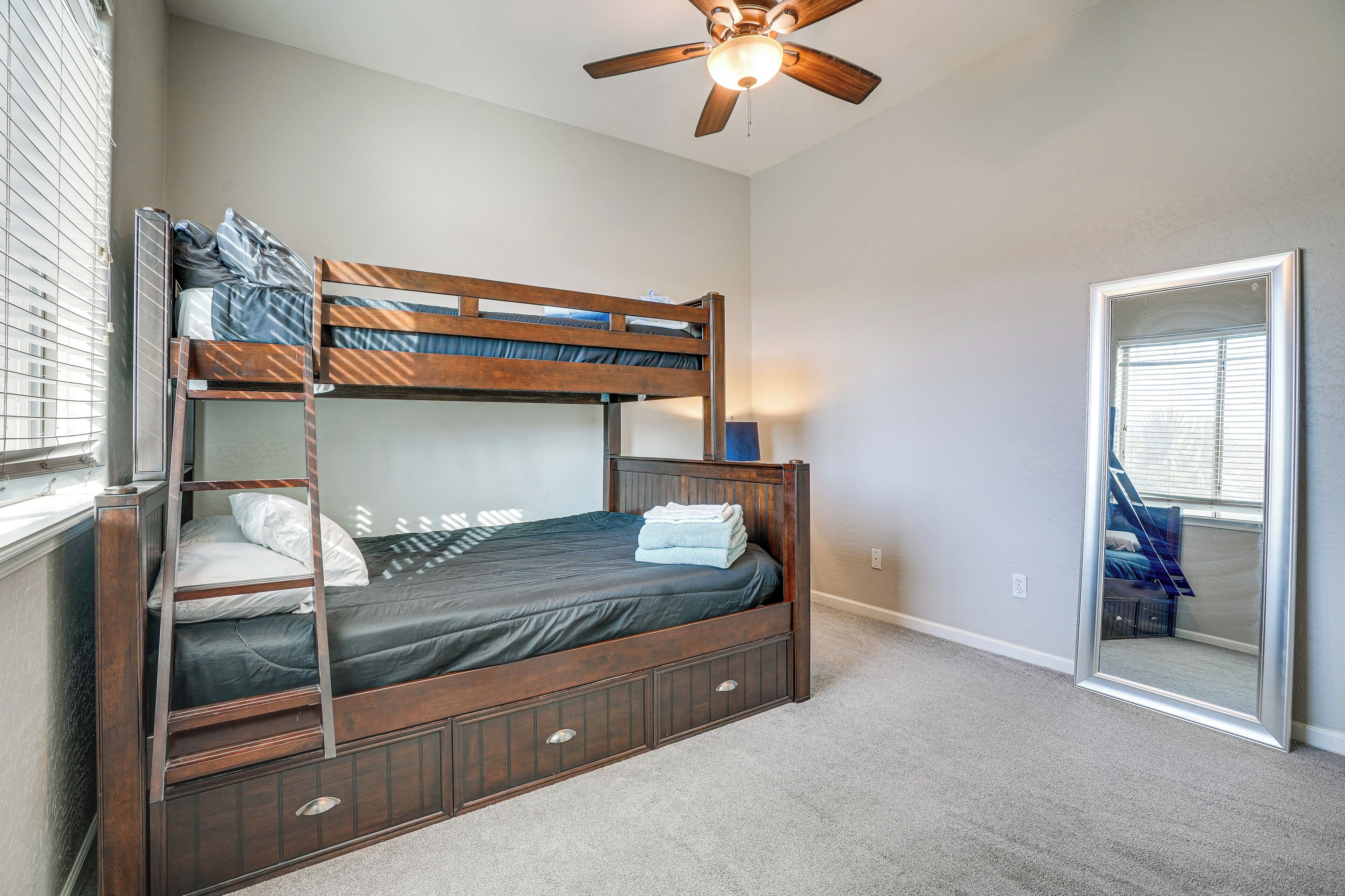 Un lit superposé avec une structure en bois, un ventilateur de plafond et un grand miroir au mur.