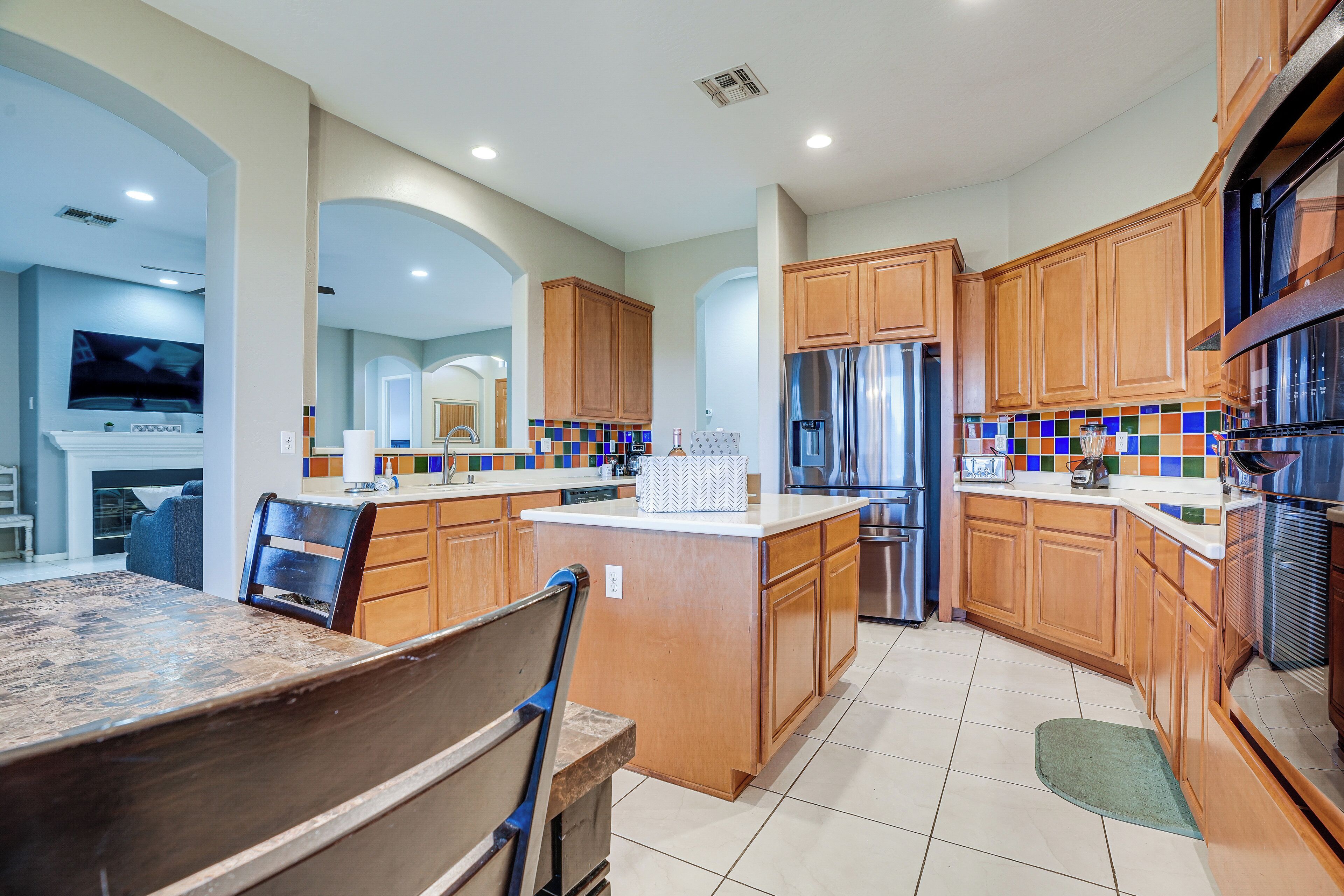 A modern kitchen with wooden cabinets, a central island, stainless steel appliances, and a tiled backsplash.