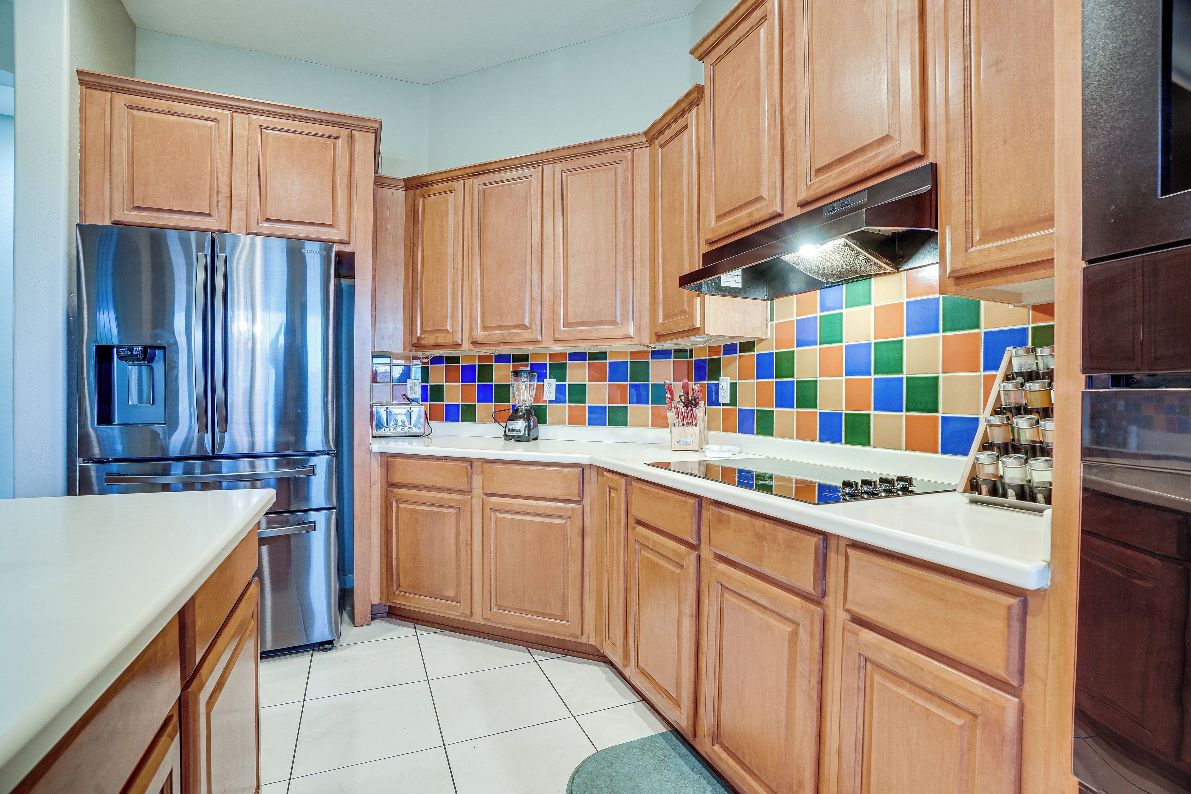 A kitchen with wooden cabinets, stainless steel appliances, and a colorful tile backsplash.