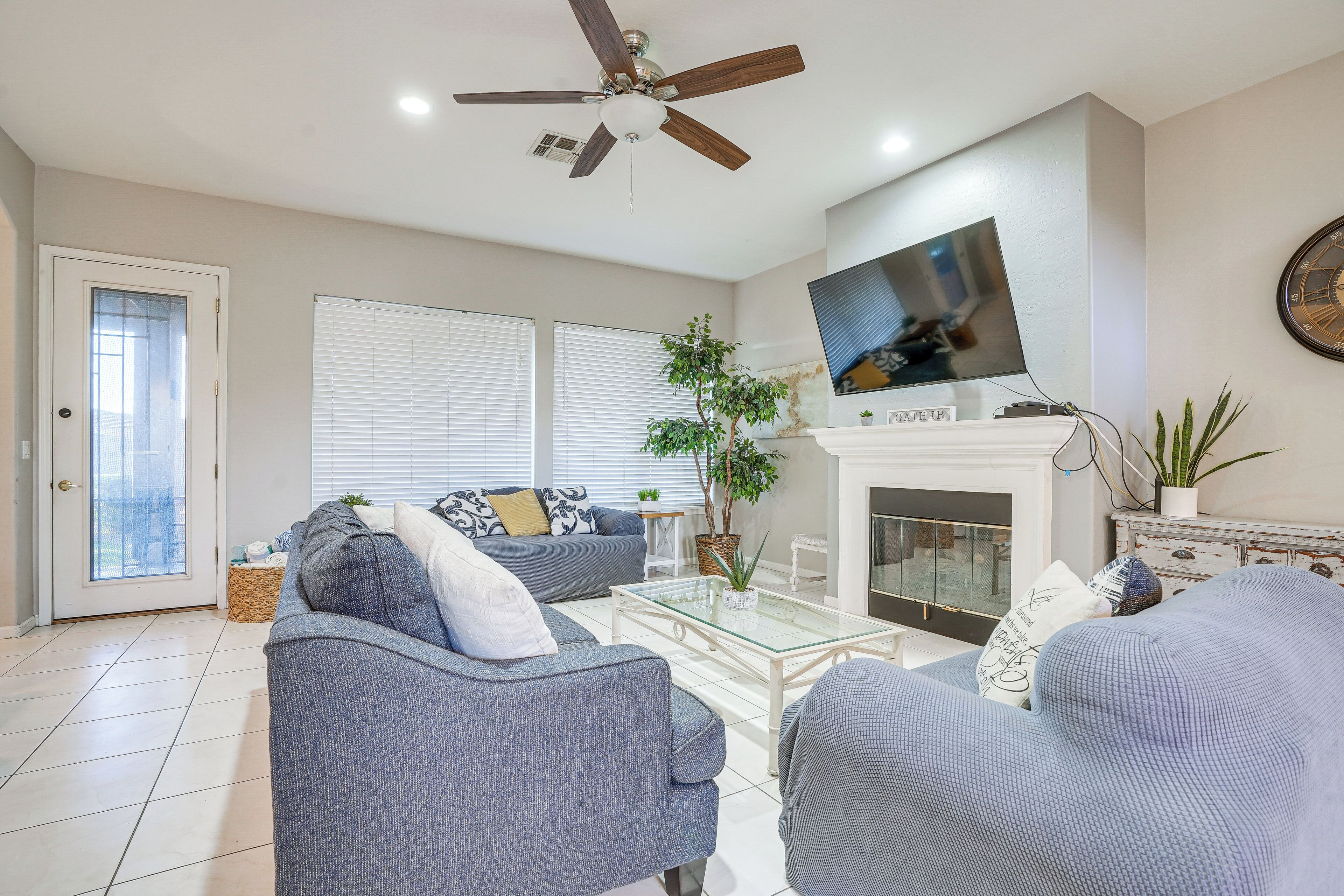 A living room with two sofas, a glass coffee table, a TV mounted above a fireplace, and a ceiling fan.