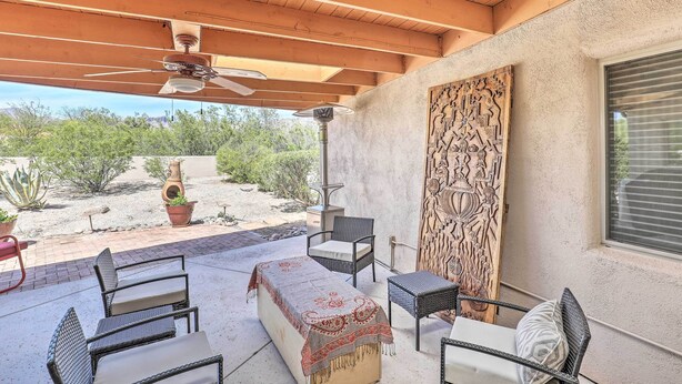 Un patio al aire libre con vigas de madera en el techo, ventiladores de techo y diferentes opciones de asientos, incluyendo sillas de mimbre y un banco.