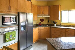 A kitchen with wooden cabinets, a stainless steel refrigerator, a microwave, and a granite countertop. - Tucson Home w/ Patio - Near Outdoor Adventure (Tucson)
