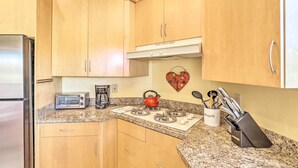 Una cocina con armarios de madera, un refrigerador de acero inoxidable, un tostador, una tetera, una estufa a gas y un bloque de cuchillos.