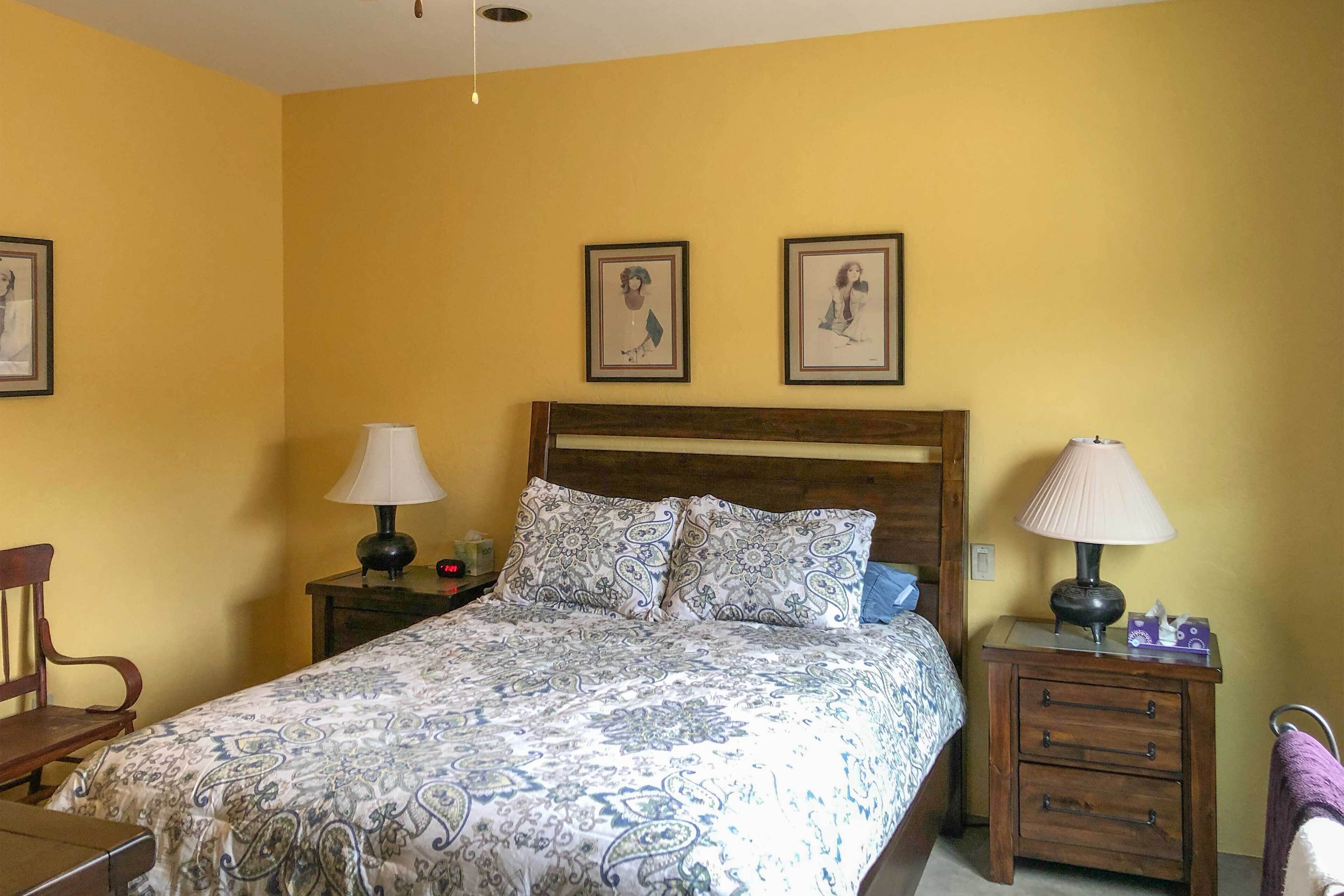 A bedroom with a bed, two nightstands, a wooden headboard, and two framed pictures on the wall.