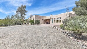 Una casa moderna con entrada de grava, rodeada de vegetación desértica y un cielo azul despejado.