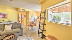 Una sala de estar con un sofá, una mesa de centro, una mesa de comedor con sillas, una escalera y una ventana con persianas.