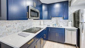 A modern kitchen with dark blue cabinets, stainless steel appliances, and a white marble countertop. - Sleek Coastal Abode: 1 Block to Naples Beach! (Naples)