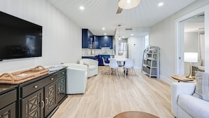 A modern living room with a flat-screen TV, a ceiling fan, and a dining area with a table and chairs. - Sleek Coastal Abode: 1 Block to Naples Beach! (Naples)