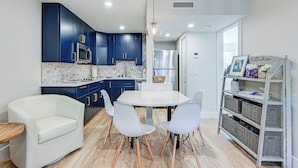 A modern kitchen with dark blue cabinets, a white dining table, and white chairs. - Sleek Coastal Abode: 1 Block to Naples Beach! (Naples)