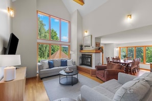 A spacious living area with a fireplace, large windows, and a dining table. - Private Hot Tub + Game Room: Galena Territory Home (Galena)