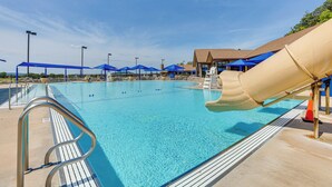 Une piscine avec un toboggan, des parasols bleus et un poste de surveillance pour les sauveteurs.