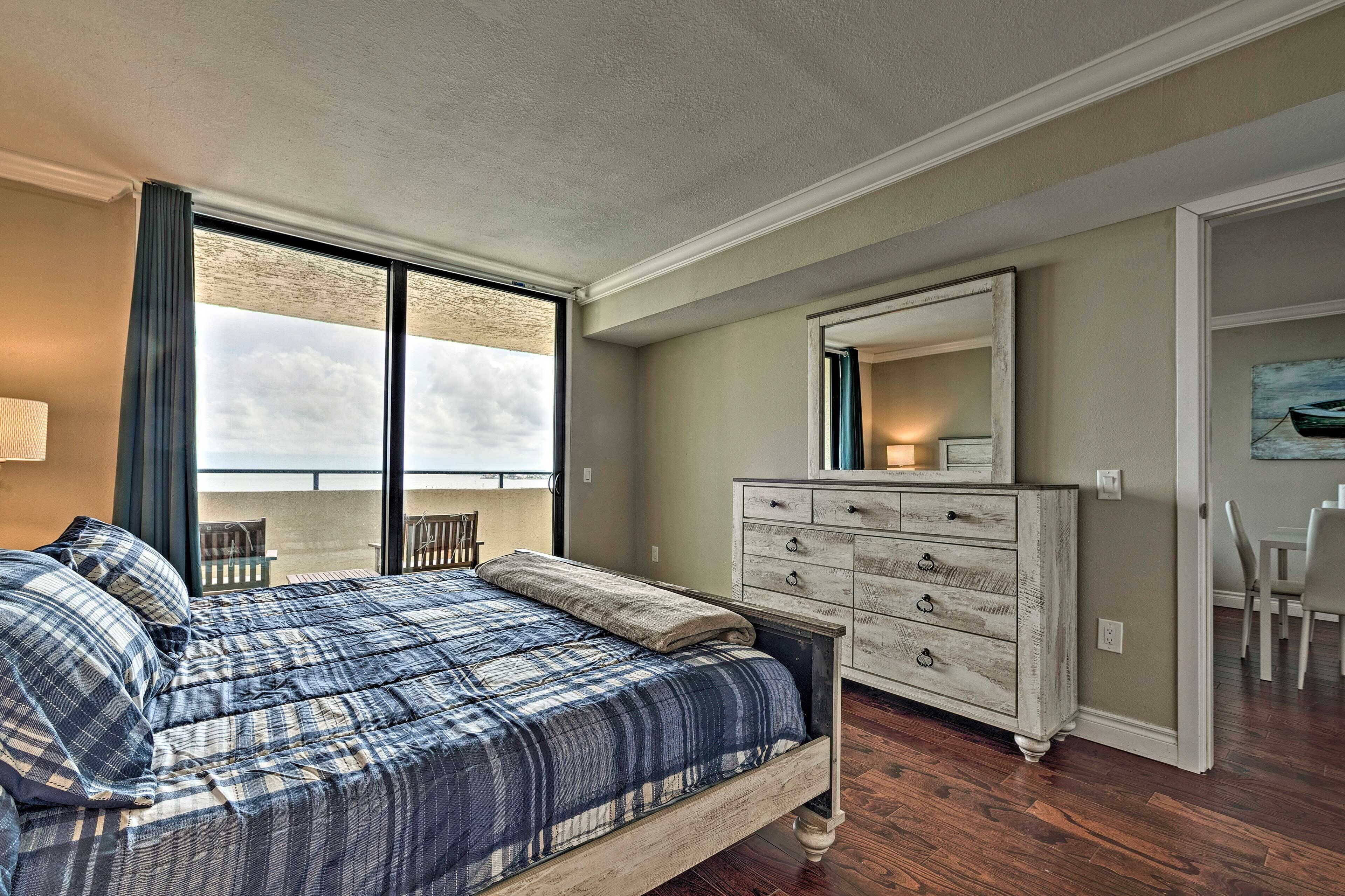 A bedroom with a large bed, a dresser, a mirror, and a balcony view.