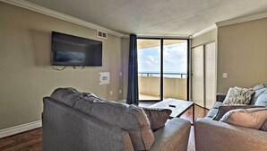 A living room with a flat-screen TV mounted on the wall, a gray sofa, a smaller gray armchair, and a coffee table. - Private Beach Access: Hudson Resort Condo! (Hudson)