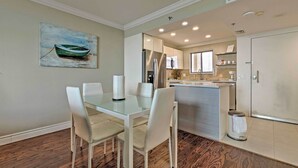 A dining area with a glass table and white chairs, a kitchen with stainless steel appliances, and a painting of a boat on the wall. - Private Beach Access: Hudson Resort Condo! (Hudson)
