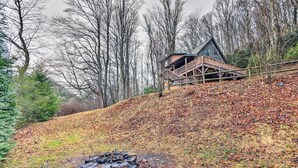 Eine Holzhütte mit einer Holzterrasse und einem Steinkamin in bewaldeter Landschaft.