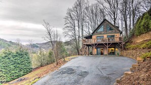 Eine zweistöckige Blockhütte mit Balkon, umgeben von Bäumen und einem Berg im Hintergrund.