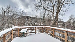 A snow-covered deck with a wooden railing and a single table. - Spacious Irwin Home on Snake River! (Irwin)