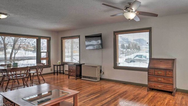 A spacious living room with hardwood floors, a ceiling fan, a dining area with a wooden table and chairs, and large windows with blinds. - Spacious Irwin Home on Snake River! (Irwin)