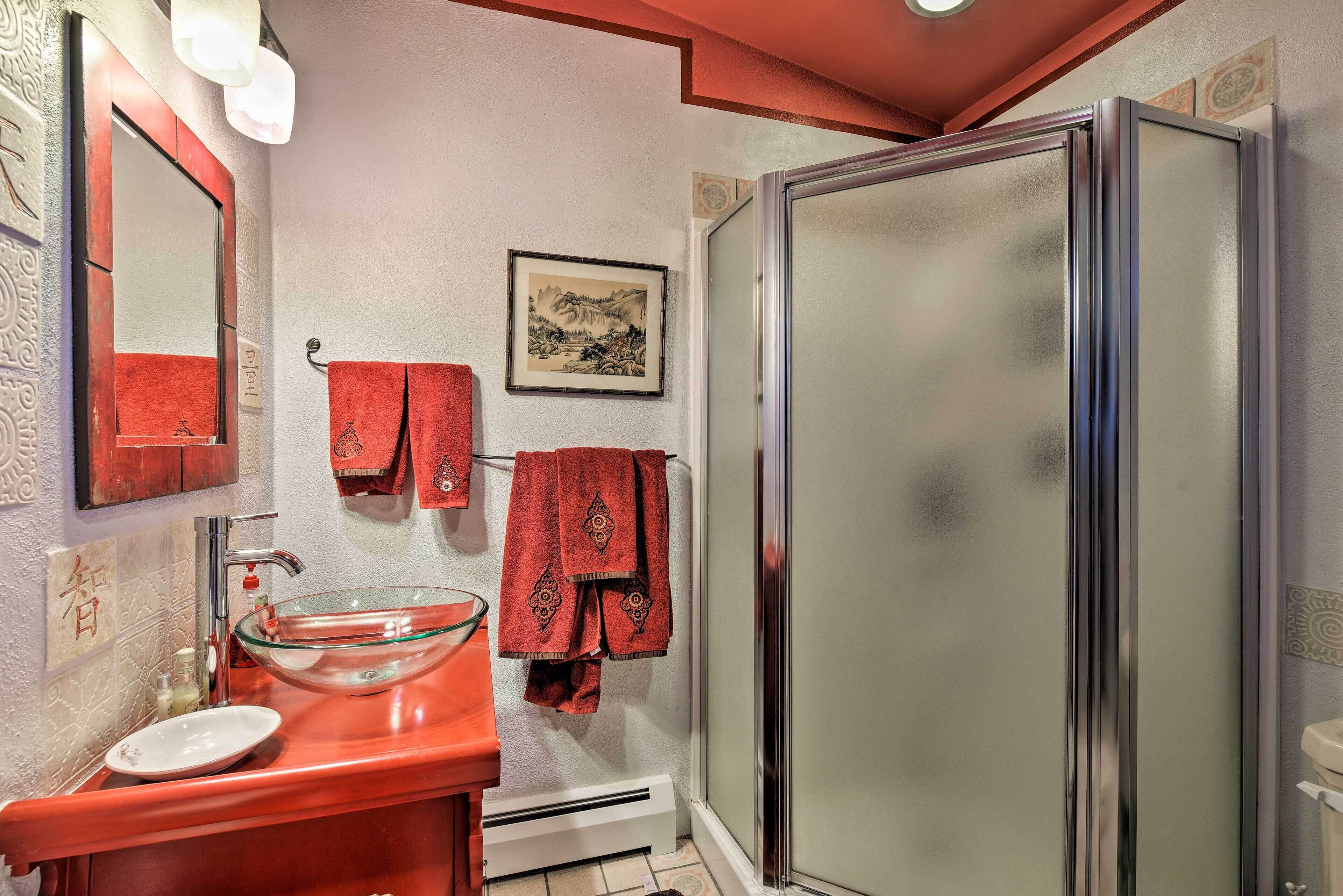 A bathroom with a glass bowl sink, a shower with frosted glass doors, and red towels hanging on hooks.
