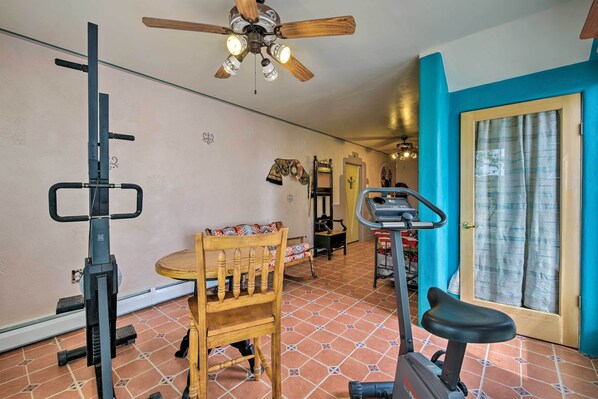 A home gym with exercise equipment, a ceiling fan, and a door with curtains.