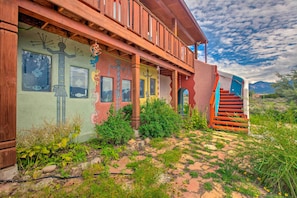 A building with a wooden balcony, a staircase, and a mural with abstract figures. - Taos Area Escape on 1.5 Acres: Panoramic Mtn Views (El Prado)