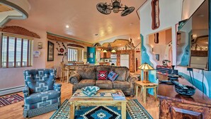 A spacious living room with a brown leather sofa, a patterned armchair, and a wooden coffee table. - Taos Area Escape on 1.5 Acres: Panoramic Mtn Views (El Prado)