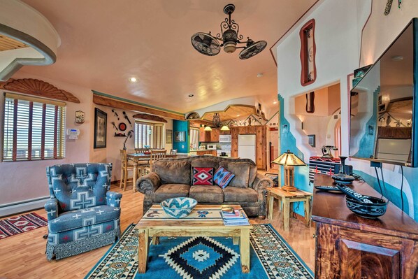 A spacious living room with a sofa, armchair, and coffee table, featuring a chandelier and decorative items. - Taos Area Escape on 1.5 Acres: Panoramic Mtn Views (El Prado)
