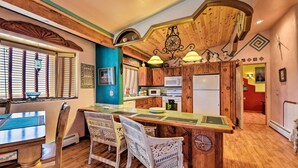 A kitchen with wooden cabinets, a central island, and a dining area with chairs. - Taos Area Escape on 1.5 Acres: Panoramic Mtn Views (El Prado)