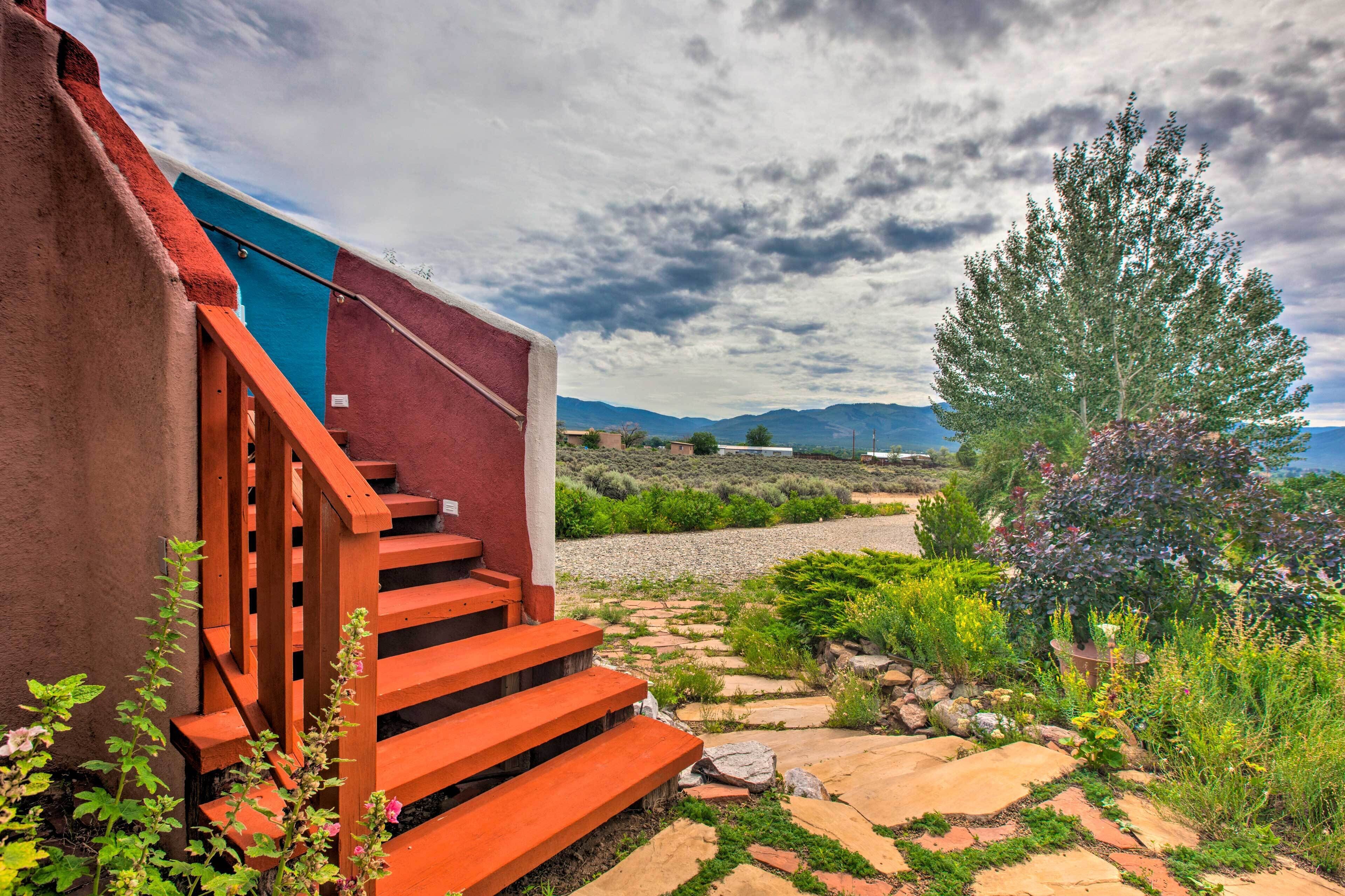 A staircase leading to a building with a view of a garden and mountains in the background.