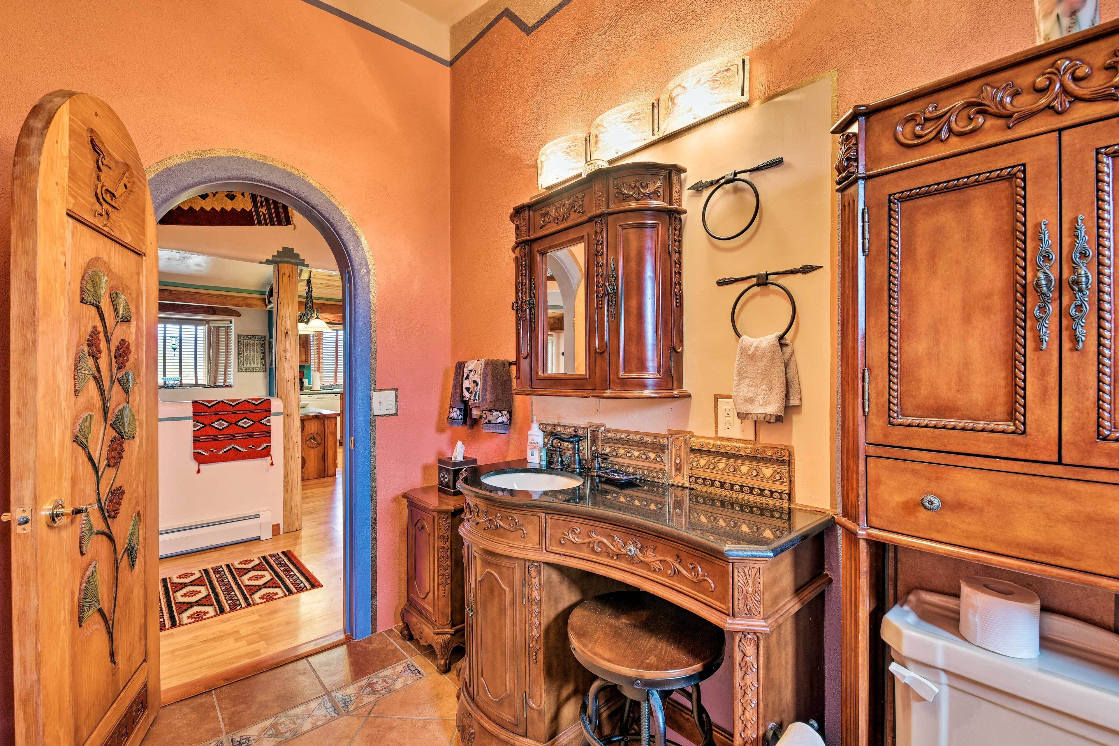 Un baño con tocador de madera, un lavabo y un inodoro. Hay un espejo sobre el lavabo y una toalla colgada en la pared.