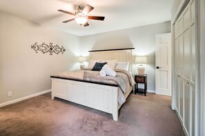 A bedroom with a bed, a ceiling fan, a wall decor, a nightstand, and a door. - Relax Poolside! Family Getaway in Nashville Area (Pegram)