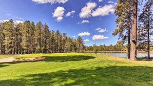 A golf course with a pond, surrounded by tall pine trees and a clear blue sky. - Deck + Fireplace: Cozy Pinetop Lakes Cabin! (Pinetop)