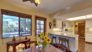 A kitchen with a central island, wooden chairs, a dining table, and a vase with sunflowers. - Deck + Fireplace: Cozy Pinetop Lakes Cabin! (Pinetop)
