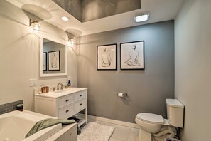 A modern bathroom with a bathtub, sink, and toilet. There are framed wall art pieces and a mirror above the sink. - The Barn House: Caldwell Mtn Retreat w/ Hot Tub! (Caldwell)